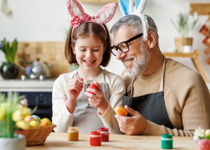 Happy little girl granddaughter dye Easter eggs with grandfather
